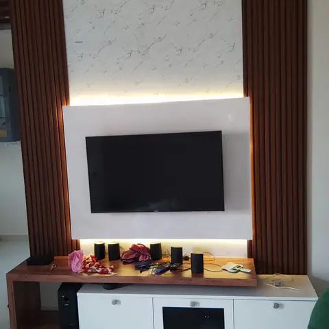 Living room TV wall with fluted wood side panels framing a marble-clad backdrop and a floating white TV panel with cove lighting, wood console below.