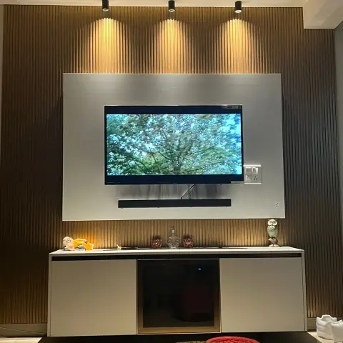 Living room TV wall with fluted wood panelling and a brushed-steel accent panel behind the screen, spotlighted from