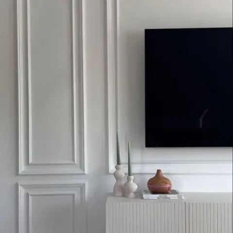 Living room TV wall with tall white panel moulding, a fluted floating TV console styled with ceramic vases, candles, and stacked books