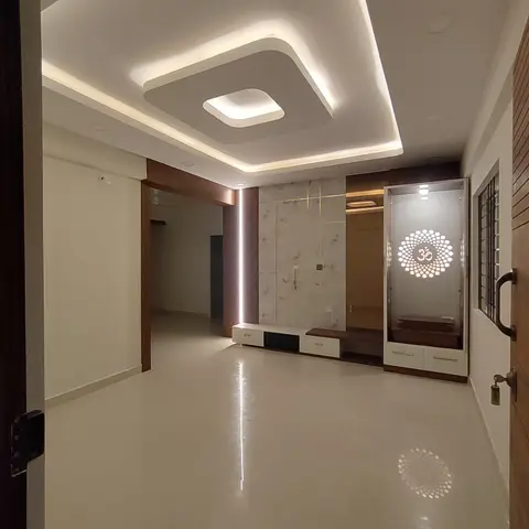 Living room TV wall with veined marble cladding and LED profile lighting, beside a backlit pooja unit with a laser-cut Om lotus motif.