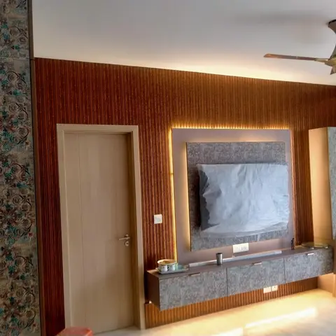 Living room TV wall with vertical reeded wood panelling and a backlit niche around a plastic-wrapped television
