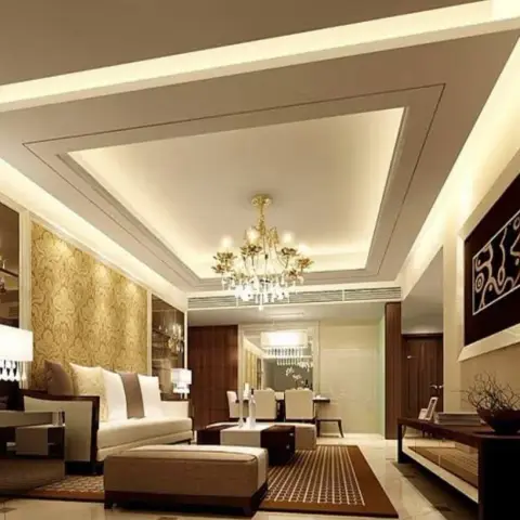 Living room under a deep multi-step cove-lit ceiling, a gilt crystal chandelier hanging over dark-framed cream sofas with a gold damask panel edged in bronze