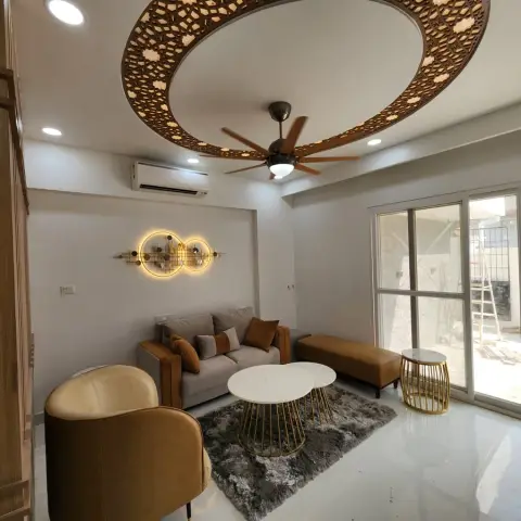 Living room under a large circular ceiling drop ringed with backlit CNC-cut walnut jaali, with a wooden-bladed fan at its centre over a beige sofa