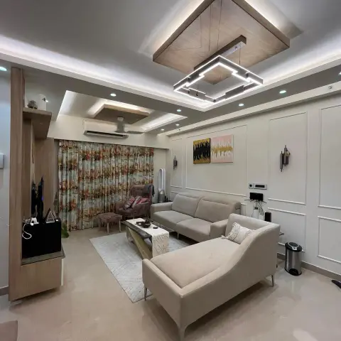 Living room under a wood-clad ceiling raft holding a squared LED profile pendant, with beige fabric sofa and chaise on a cream rug