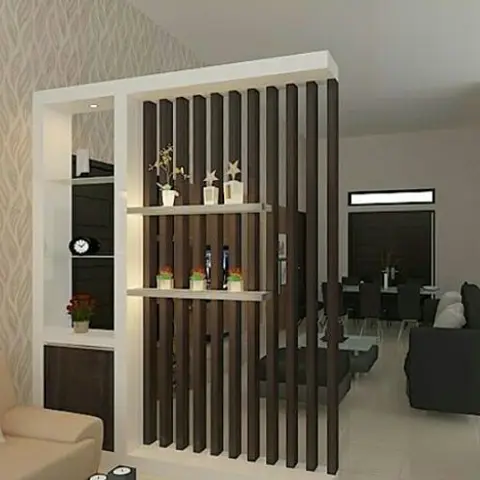 Living room viewed through a fluted wood-slat partition with styled display ledges, beige sofa in the foreground and a black sofa and dining set beyond