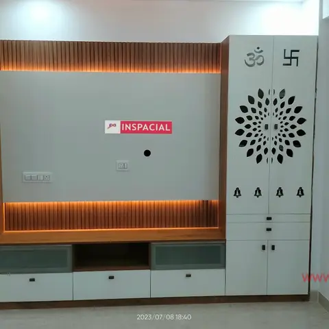 Living room wall combining a fluted wood-panelled TV backdrop with an open ladder display shelf on one side and a white carved-jaali pooja cabinet with Om