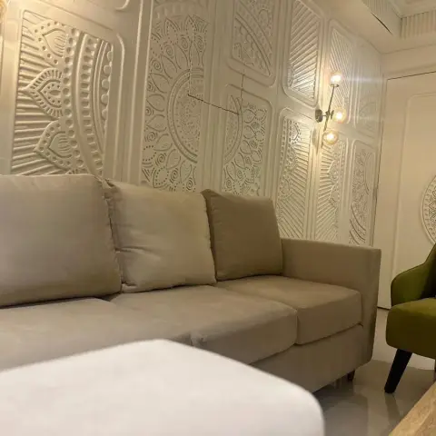 Living room walled floor-to-ceiling in white carved mandala relief panels, with a beige L-shaped fabric sofa