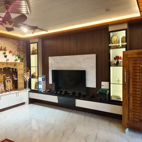 Living room where a dark fluted TV wall with a white marble slab and two backlit glass display columns meets a carved teak pooja mandir stepped in white