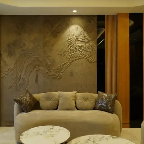 Living room where a hand-sculpted flowing-relief plaster panel is grazed by a single spotlight behind a curved beige velvet sofa