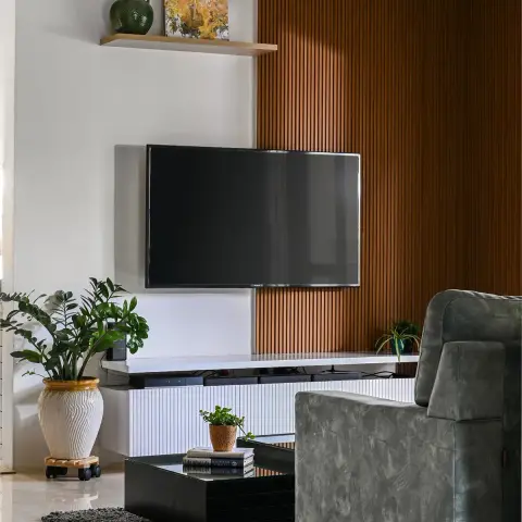 Living room where a wall-mounted TV sits on white plaster beside a full-height teak slat panel, over a white fluted console