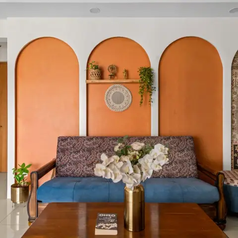 Living room where three terracotta arches are painted straight onto the white wall behind a wooden-armed sofa upholstered in blue and paisley