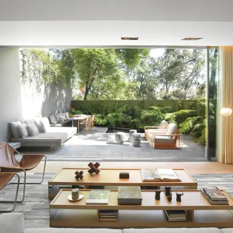 Living room whose full-width glazed wall slides right back to a fern-planted deck, with two brown leather sling chairs