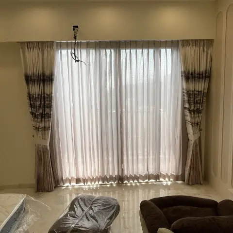 Living-room window dressed in sheer white pinch-pleat sheers with ombre-printed side drapes and tiebacks