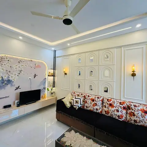 Living room with a backlit cherry-blossom mural TV wall and an arched moulded panel accent wall behind a black floral-print sofa.