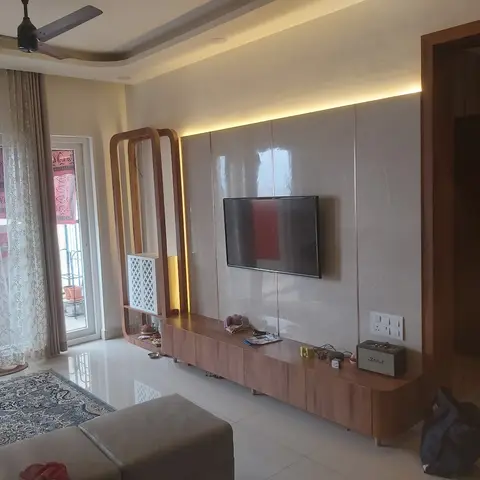 Living room with a backlit marble-effect TV wall panel, a tapered-leg wood console, and a decorative wooden arch shelf beside sheer balcony curtains.