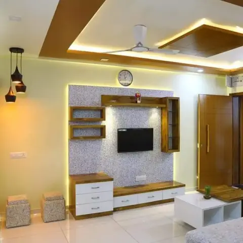 Living room with a backlit silver-textured panel carrying the TV between floating teak shelves and a small glazed wall cabinet