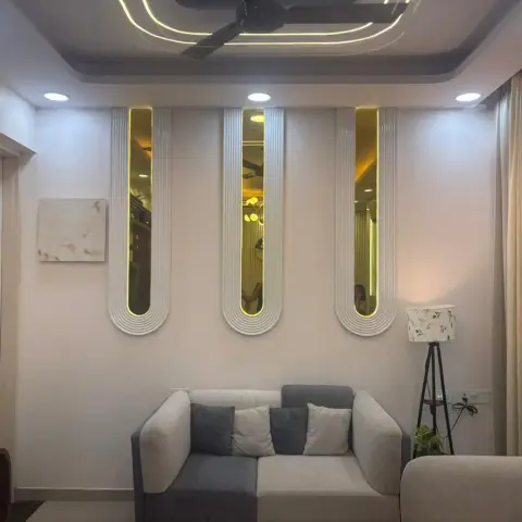 Living room with a backlit trio of arched fluted mirrors on the wall above a grey sofa, cove-lit ceiling and floor-length gold curtains.