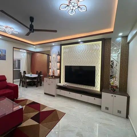 Living room with a backlit wave-textured TV feature wall flanked by a mirrored jaali strip, a maroon sofa, and a geometric triangle-pattern rug