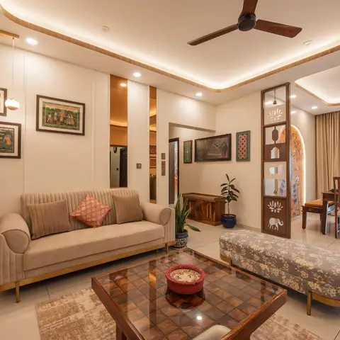 Living room with a beige channel-tufted sofa and a wood coffee table, facing a carved jaali partition with lotus and elephant motifs that screens the dining