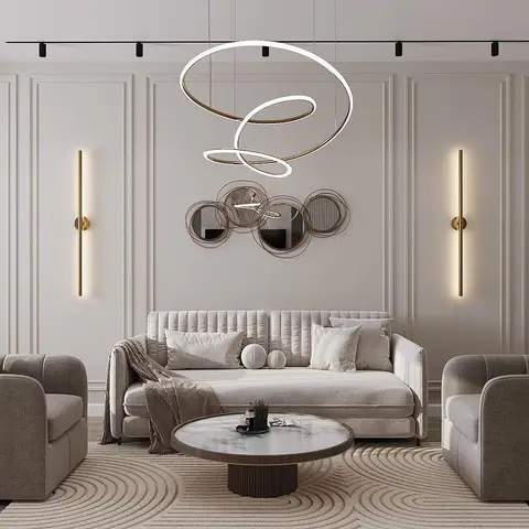 Living room with a beige channel-tufted sofa flanked by two barrel armchairs, a cluster of round mirrors and a swirling ring pendant light on a panelled wall.