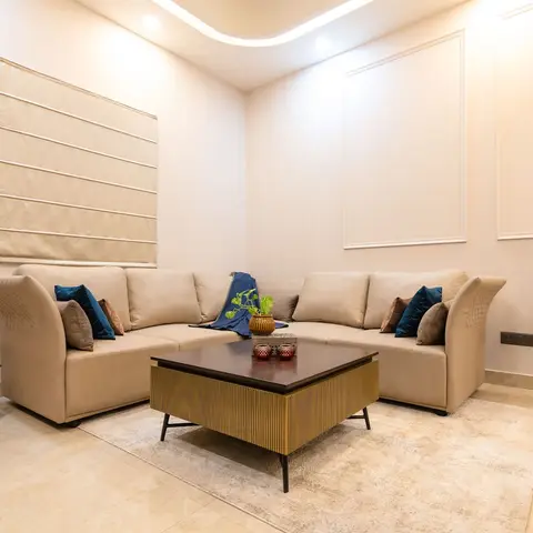 Living room with a beige L-shaped sofa in teal and mustard cushions, a fluted-base coffee table with wood top, curved cove ceiling