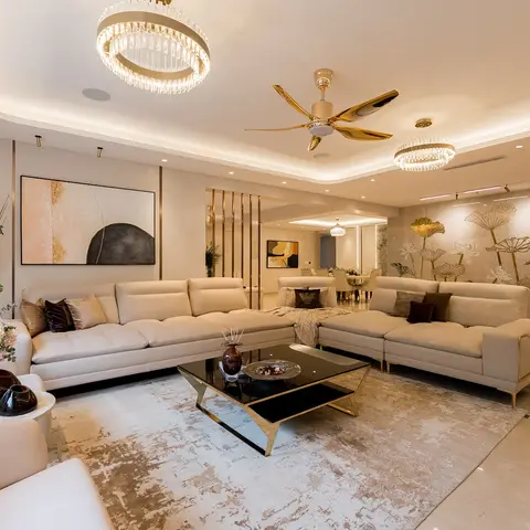 Living room with a beige L-shaped leather sectional, dual crystal ring chandeliers, a gold ceiling fan, and a gold lotus-motif stone accent wall.