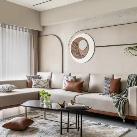 Living room with a beige L-shaped sectional sofa, tan leather and patterned cushions, a circular sculptural wall art piece on textured plaster