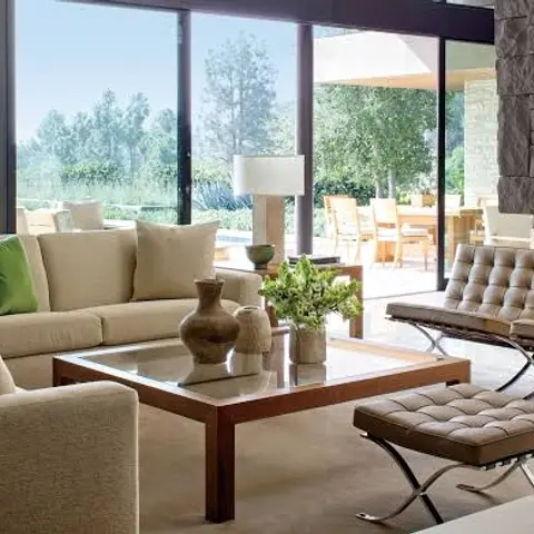 Living room with a beige sectional sofa and tan leather Barcelona chairs and ottoman around a walnut-and-glass coffee table