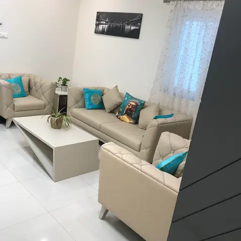 Living room with a beige tufted leather sofa set styled with teal accent cushions, a white geometric coffee table
