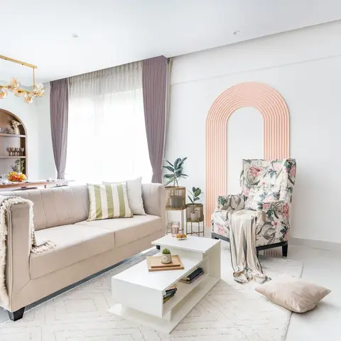Living room with a beige tufted sofa and a floral wingback chair set against a blush arched wall panel, under a gold sputnik chandelier