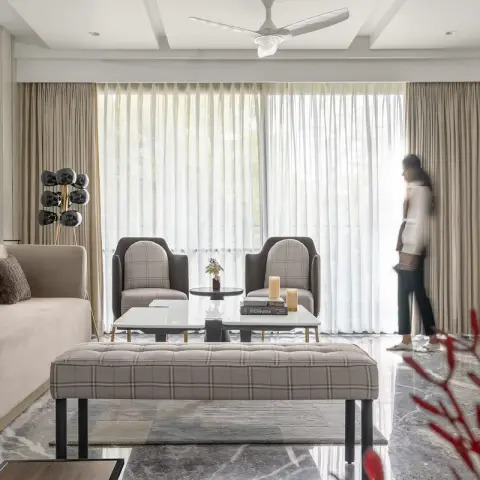 Living room with a beige velvet sofa facing two checked-wool tub chairs, a long tufted bench on black legs and paired white marble coffee tables