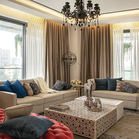 Living room with a black candelabra chandelier, layered gold curtains, cream sofas styled with navy and patterned cushions