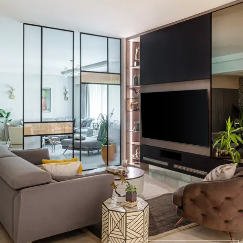 Living room with a black lacquer TV wall and backlit wood-veneer display shelving, grey velvet sofa and a tufted brown armchair