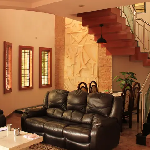 Living room with a black leather reclining sofa set, a marble coffee table, and a carved stone relief mural wall beneath the staircase.