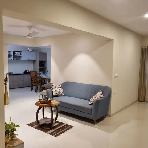 Living room with a blue channel-tufted sofa and a round wood side table, opening onto a kitchen and dining area through an archway.