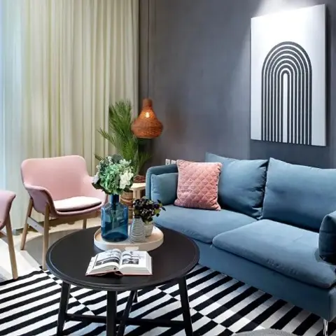 Living room with a blue velvet three-seater sofa flanked by two blush-pink armchairs around a round black coffee table