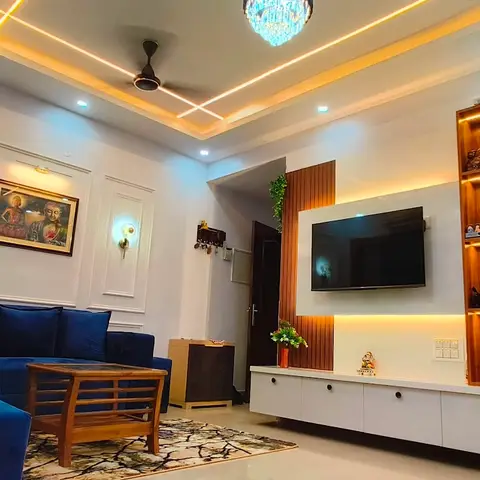 Living room with a blue velvet sofa facing a backlit wood-and-white TV unit wall, crisscross cove-lit ceiling with a crystal pendant