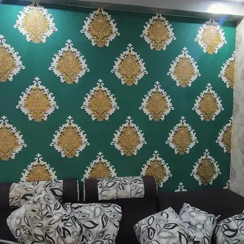 Living room with a bold emerald-and-gold damask wallpaper feature wall meeting a cream damask wallpaper side wall