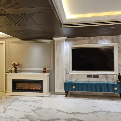 Living room with a book-matched marble TV wall framed in white moulding, a teal fluted TV console on brass-capped legs