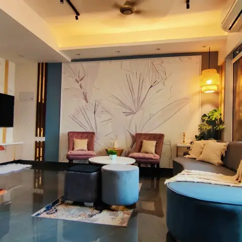 Living room with a botanical line-art wallpaper feature wall, blush-pink tufted armchairs, and a curved teal velvet sofa under rattan cage pendant lights.