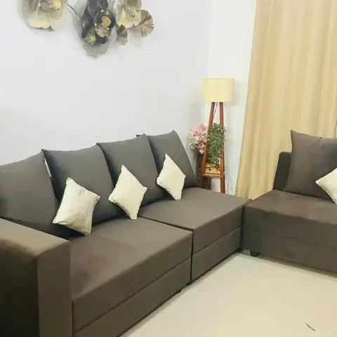 Living room with a brown fabric L-shaped sofa and matching loveseat, cream curtains, and a metal ginkgo-leaf wall sculpture above the sofa.