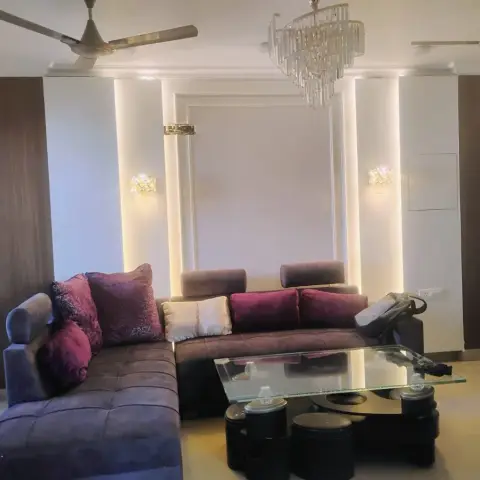 Living room with a brown suede L-sofa piled with maroon cushions facing a glass-top coffee table ringed by four black drum stools