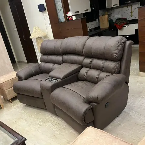 Living room with a brown suede reclining loveseat and fold-down console, opening directly into a wood-and-white modular kitchen.