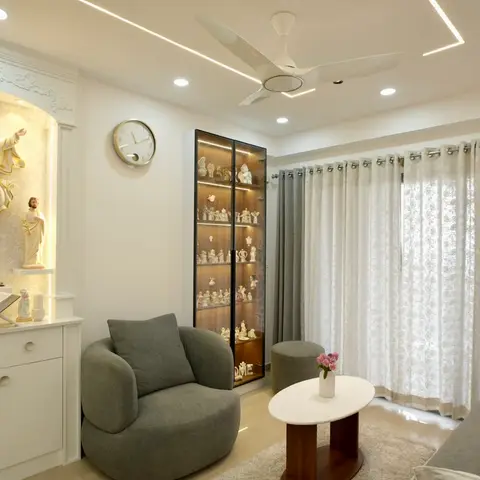 Living room with a built-in white carved prayer niche holding devotional statues beside a lit glass display cabinet