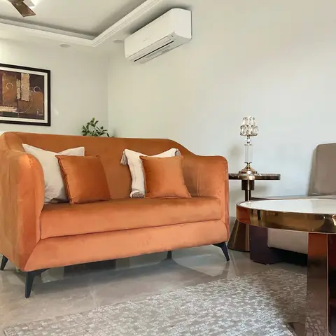 Living room with a burnt-orange velvet sofa, a round mirrored brass coffee table, and a crystal table lamp