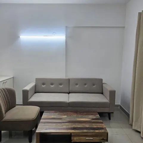 Living room with a button-tufted grey three-seater sofa, a channel-tufted accent chair, and a reclaimed-wood coffee table against a plain white wall.