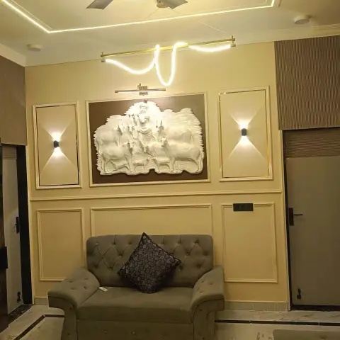 Living room with a carved relief sculpture of Krishna and cows set into a gold-trimmed moulded wall panel, flanked by wall sconces, above a tufted grey sofa.
