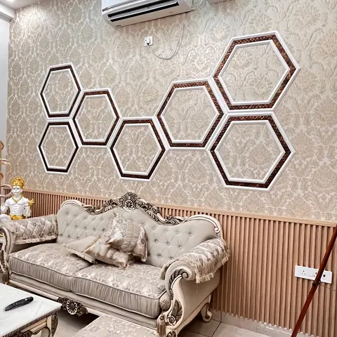 Living room with a carved wood-frame damask sofa set against beige damask wallpaper, a cluster of hexagonal wall-art frames, and a fluted wood wainscot below.