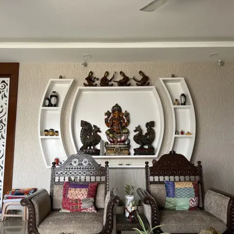 Living room with a carved wooden lion-motif jaali screen, textured wallpaper, a rounded display niche holding a Ganesha statue and brass figurines