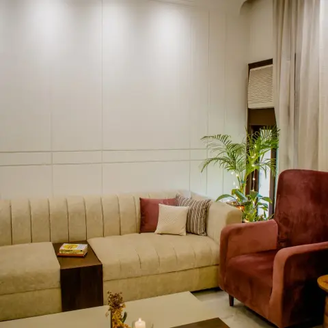 Living room with a channel-tufted beige sectional sofa built around a wood side table, a maroon velvet armchair, and a grooved panelled wall behind.